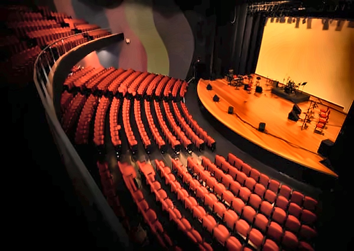 Interior do Teatro Ariano Suassuna, em Jacareí-SP: plateia com poltronas vermelhas e o palco iluminado